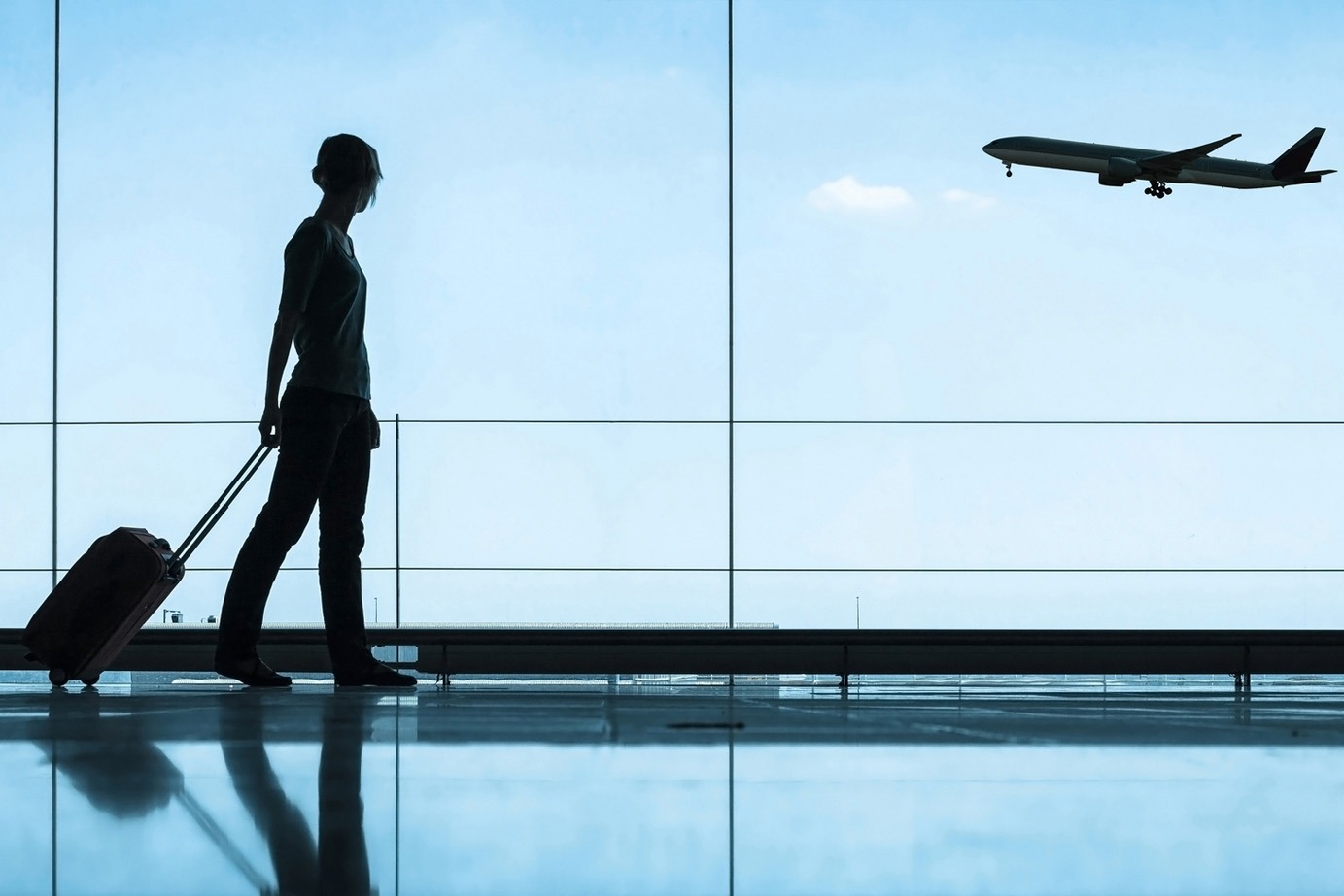 persona caminando con equipaje en el aeropuerto con avión volando en el fondo